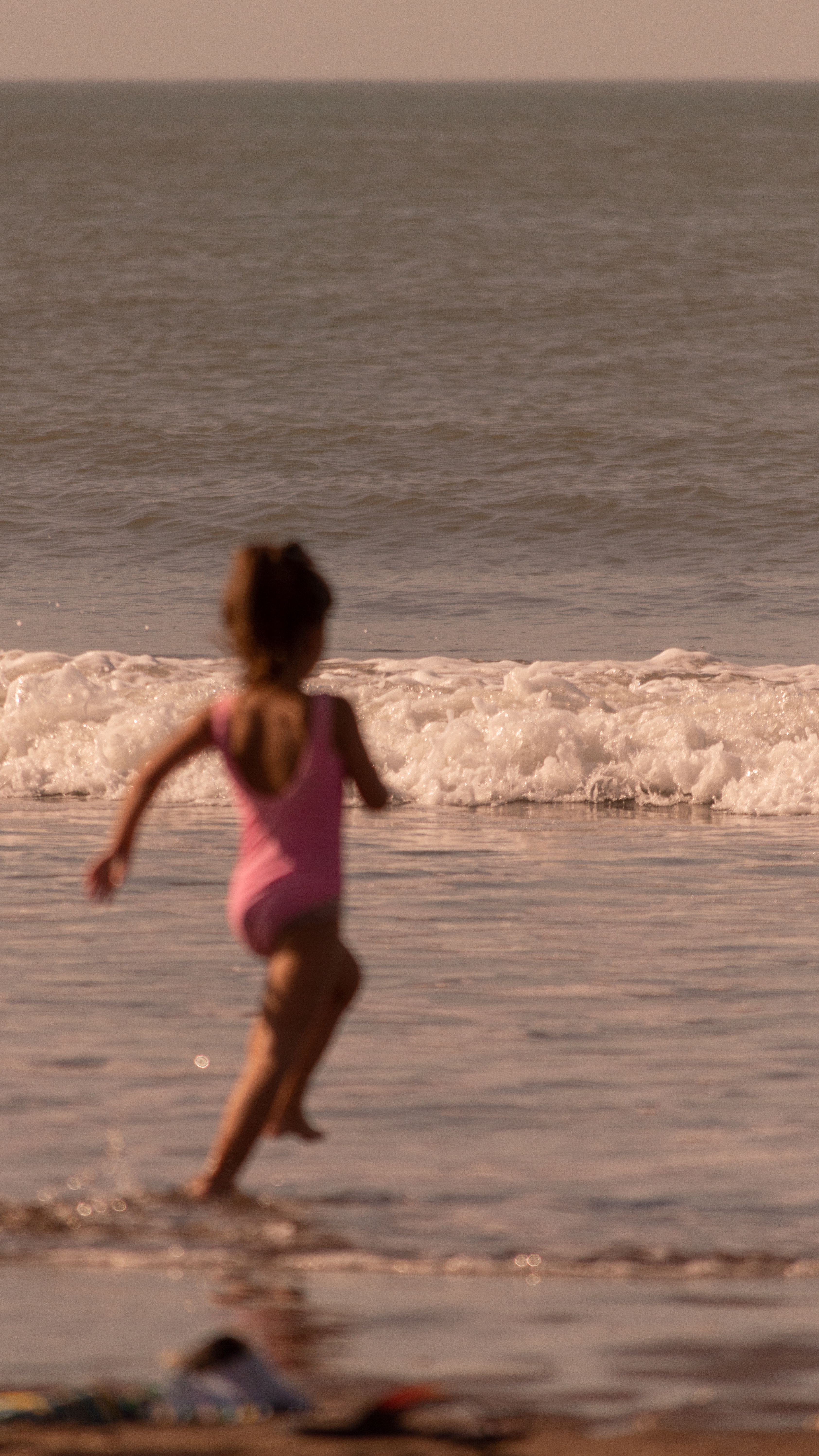Criança correndo na beira-mar ao entardecer na Praia do Rosa, Imbituba